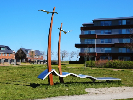 This bench is placed at a playground in a new residential area in Schagen Netherlands. Dimensions 6 meters wide, 5 meters high, 1 meter deep. Stainless steel bench. Corten steel arches with seagulls have been placed through the bank. The residential area is built on a reclaimed area. The waves in the bank symbolize the water that has been expelled and the flat ground that has arisen. The birds stand for the freedom that people live in in this district.